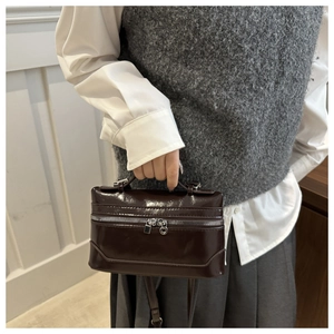 Detailed view of deep brown glossy leather mini box bag with top handle and double zippers