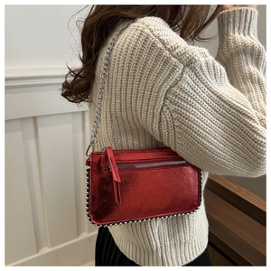 Detail of red metallic crossbody bag with silver ball studs and chain strap shown on model