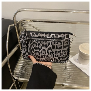 Detail showing hand holding leopard print crossbody bag with silver chain and metal studs