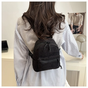 Detail of a black corduroy mini backpack on a model in a modern home interior