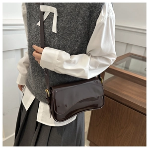 Model wearing dark brown glossy patent leather saddle bag with gold metal hardware