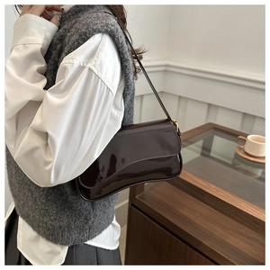Detail of dark brown patent leather underarm bag with asymmetric wavy flap and gold hardware