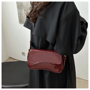 Detail of wine red patent leather shoulder bag with unique curved flap on black coat