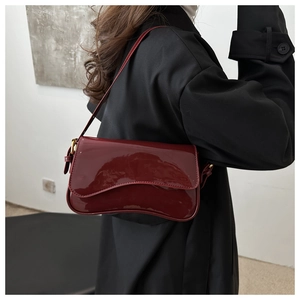 Polished wine red patent leather baguette bag shown on a model's shoulder over black coat