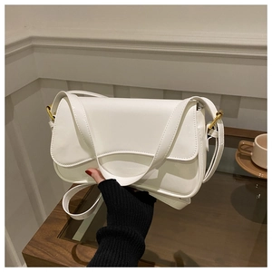 Close-up of white patent leather shoulder bag with gold metal buckle and wide strap