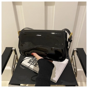 Detail of glossy black patent leather bag with curved flap and gold metal hardware buckle