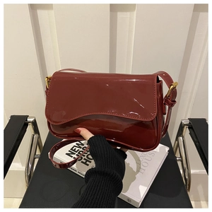 Detail view of a burgundy patent leather crossbody bag with glossy finish and gold buckle