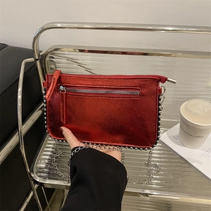 Metallic red crossbody bag with silver studs and chain strap shown in a modern setting