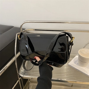 Glossy black patent leather flap shoulder bag with gold hardware held by a person