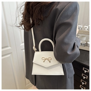 Detail of white leather mini crossbody bag with golden bow clasp shown on a model