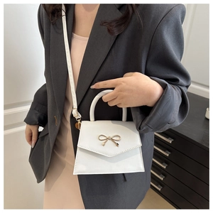 Detail of a white mini handbag with a gold bow clasp worn by a model in a gray blazer