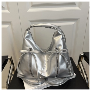 Detail der silbernen Metallic-Tasche mit vertikalen Reißverschlüssen und Schleifenbändern