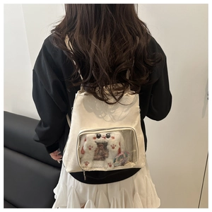 Detail of a beige ita-bag with a transparent pocket featuring a plush rabbit and charms