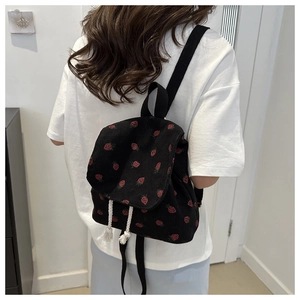 Close-up of black corduroy backpack with red strawberry pattern and tassel drawstrings