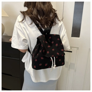 Detail of black corduroy backpack with red strawberry prints and white rope drawstring
