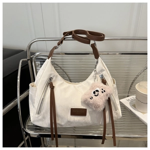 Detail of white moon bag with brown leather strap, fringe, and plush charm