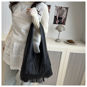 Detail showing high-quality black litchi grain leather and layered long fringe on tote bag