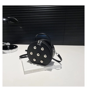 Detailansicht der runden schwarzen Ledertasche mit Nieten vor minimalistischem Hintergrund