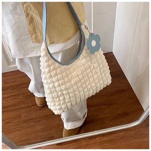 Dettaglio di una borsa a secchiello beige con ciondolo a fiore blu e tracolla chiara