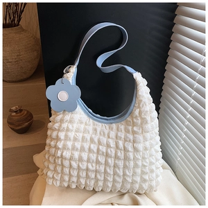 Détail du sac texturé pop-corn blanc avec bandoulière en cuir bleu et breloque fleur