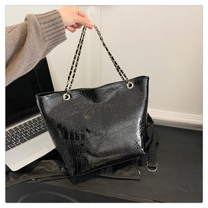 Close-up of black crocodile embossed tote bag featuring a metallic chain strap detail