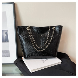 Detail of glossy black crocodile embossed tote bag with gold metal chain straps