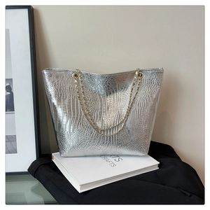 Close-up of silver tote bag with embossed crocodile texture and woven chain straps