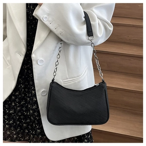 Detail of black textured moon bag with silver chain strap shown on a white blazer outfit