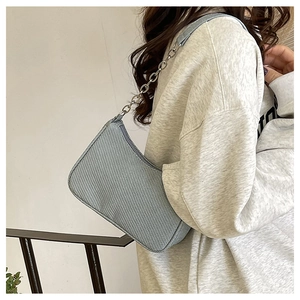 Detail of light blue textured baguette bag with silver chain strap on a female model