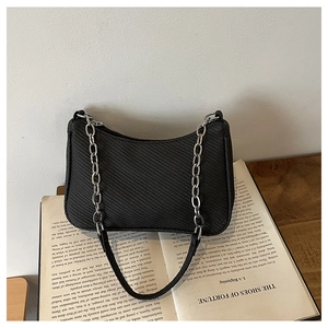 Detail of black textured baguette bag with silver chain handle on an open book