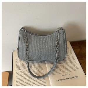 Detail of grey structured shoulder bag with twill texture and silver chain on a book