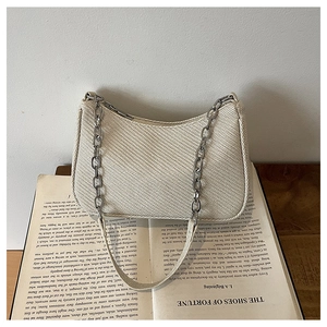 Detailed close-up of cream woven shoulder bag texture with silver chain on vintage book