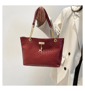 Close-up of red woven tote bag featuring a gold deer charm and chain strap details