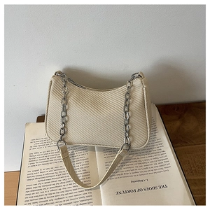 Close-up of beige woven texture handbag with silver chain on a vintage book