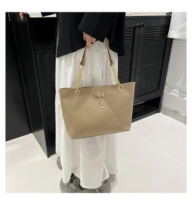Close-up of light brown woven tote bag with gold chain strap and deer charm detail
