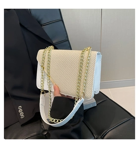 Detail of white leather trim and straw woven texture on a flap crossbody bag with gold chain