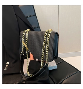 Detailed macro view of black crossbody bag with twill texture and golden chain strap