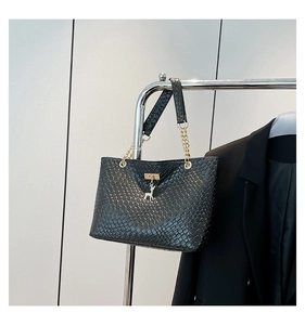 Detail of black woven texture tote bag featuring golden deer pendant and chain strap