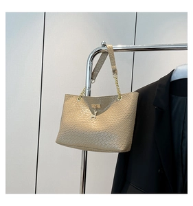 Detail of beige woven texture tote bag featuring a gold deer pendant and chain strap