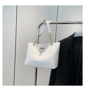 Close-up of white woven tote bag with gold deer charm and elegant chain strap detail