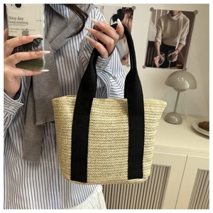 Close-up of woven straw tote bag featuring detailed texture and black canvas handles
