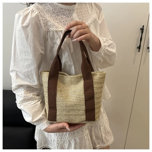 Close-up of woven straw tote bag featuring brown canvas handles and herringbone texture