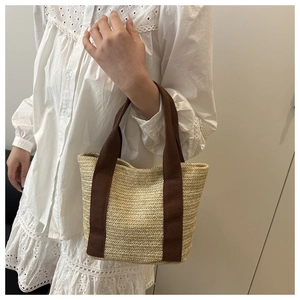 Detail of woven straw tote bag with brown fabric handles and natural texture