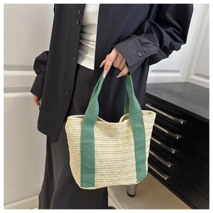 Detail of woven straw tote bag featuring beige herringbone texture and green fabric handles
