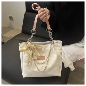 Detail of cream tote bag with pink handles, lace bow, and pearl chain pendant