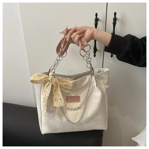 Detail of off-white tote bag with lace bow, pearl chain and pink leather handles