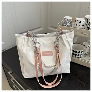 Detail of white tote bag featuring silver chain, pearl charm and pink fashion label