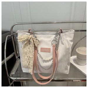 Detail of white tote bag with pink straps, lace bow, pearl charms and silver chain