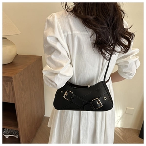 Detail view of the sleek black underarm bag featuring distinctive gold metal buckles and folds