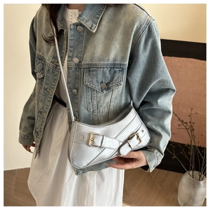 Close-up of metallic silver underarm bag with decorative buckles worn on a denim jacket